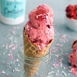 red velvet cookie dough ice cream in a cone sitting in a jar with sprinkles all around.