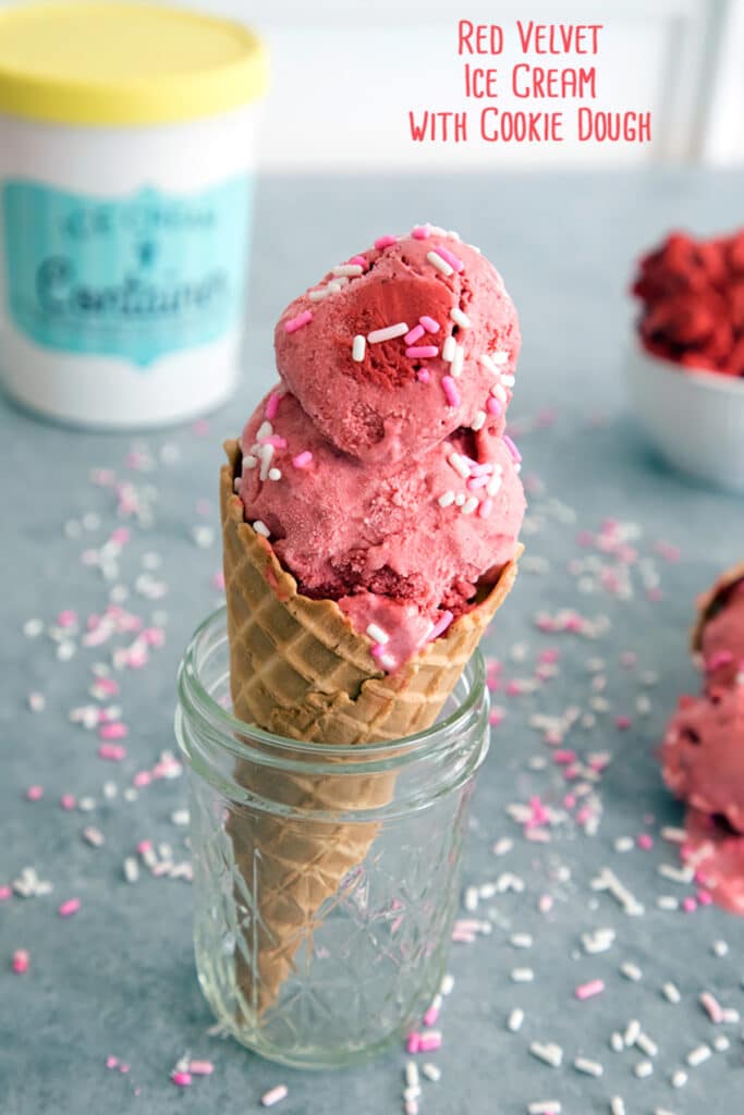 Head-on view of red velvet ice cream with cookie dough in an ice cream cone sitting in a mason jar surrounded by sprinkles and a ice cream container with recipe title at top.