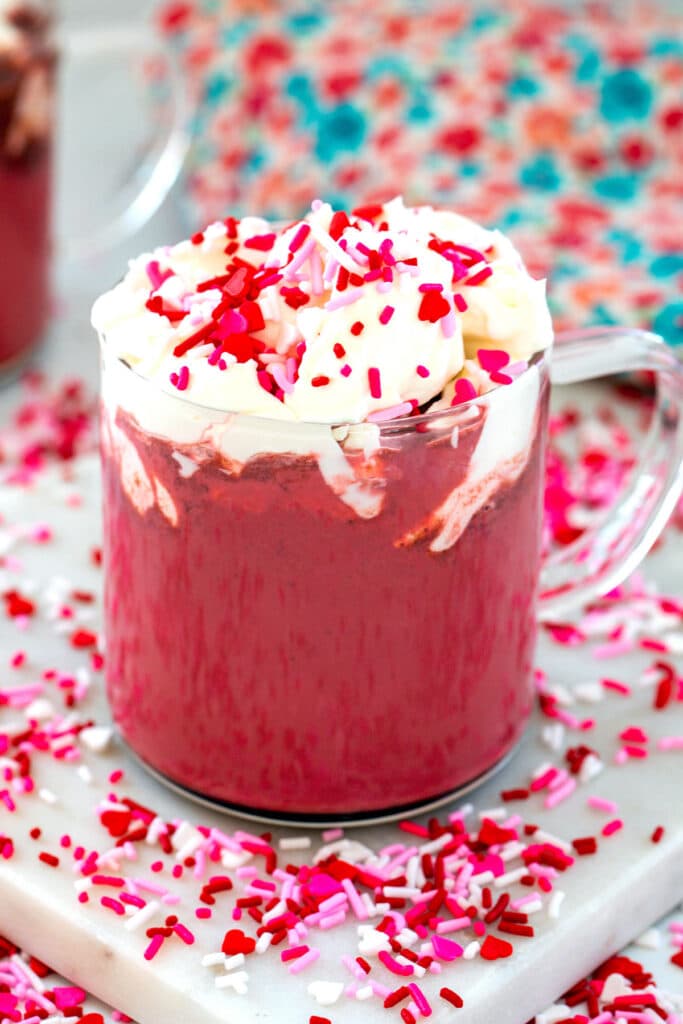 Head-on view of red velvet latte with cream cheese whipped cream and red and pink sprinkles.
