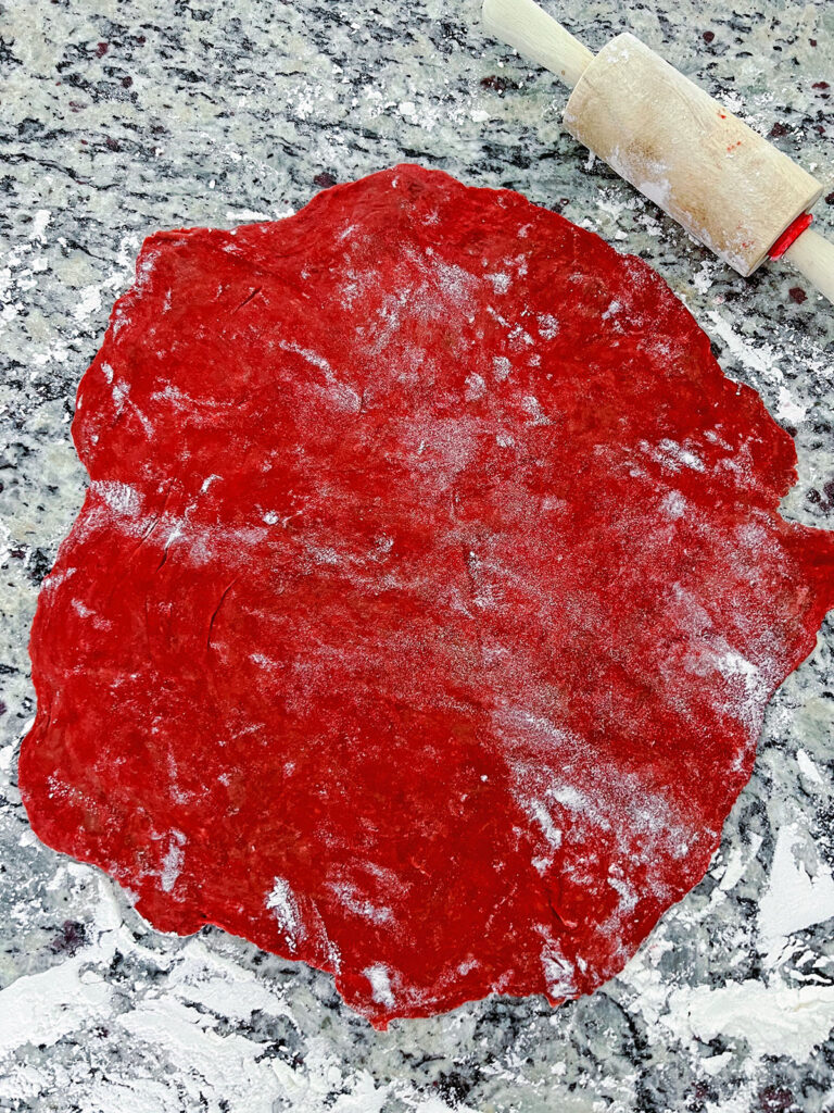 Red velvet pop tart dough rolled out in flour with rolling pin.