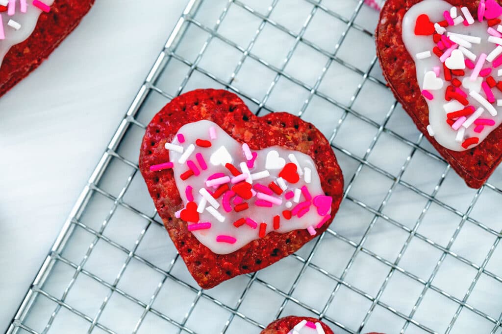 Landscape overhead view of a heart-shaped red velvet pop tart with icing and sprinkles.
