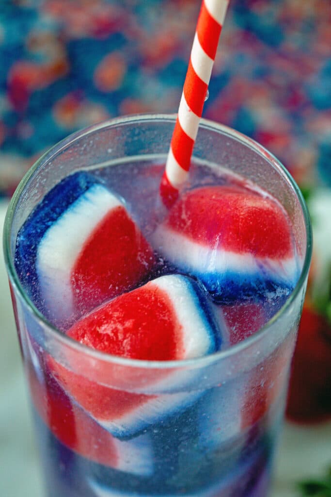 Overhead view of red, white, and blue ice cubes in a glass of soda water with red and white straw
