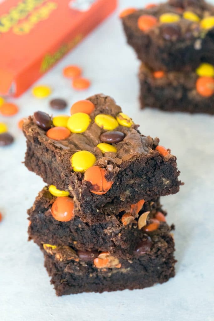 Overhead view of stack of three Reese's Pieces peanut butter brownies with Reese's Pieces and more brownies in background