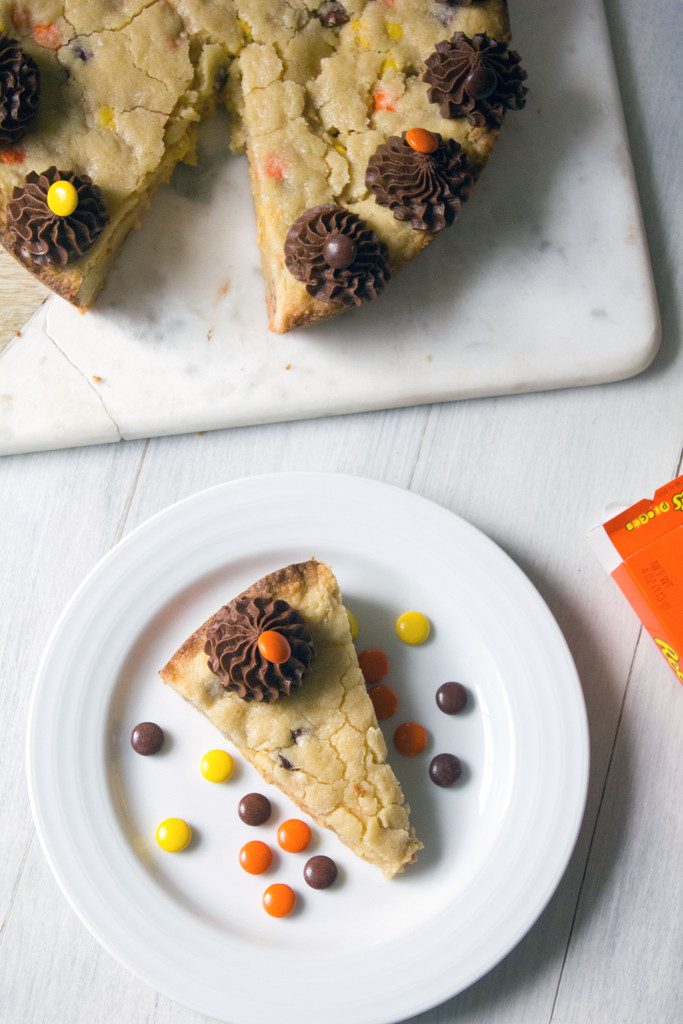 Bird's eye view of a slice of Reese's Pieces cookie cake on a white plate with rest of cookie cake on a platter