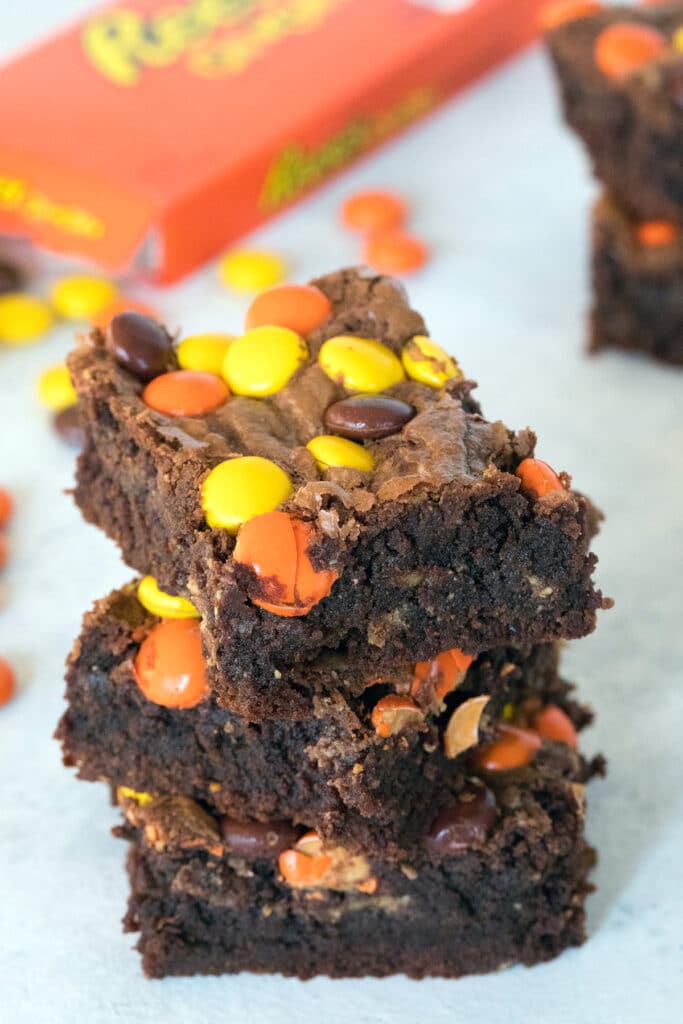 Head-on view of a stack of three Reese's Pieces peanut butter brownies with box of Reese's Pieces in the background