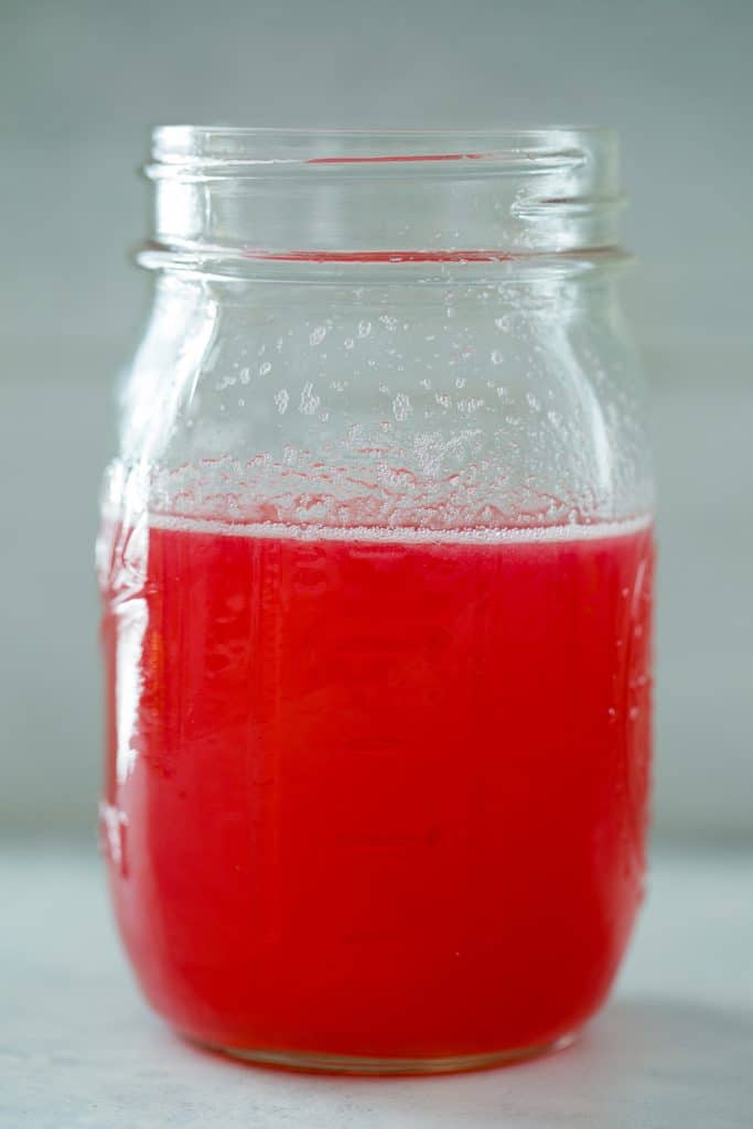 Head-on view of bright pink rhubarb simple syrup in a mason jar