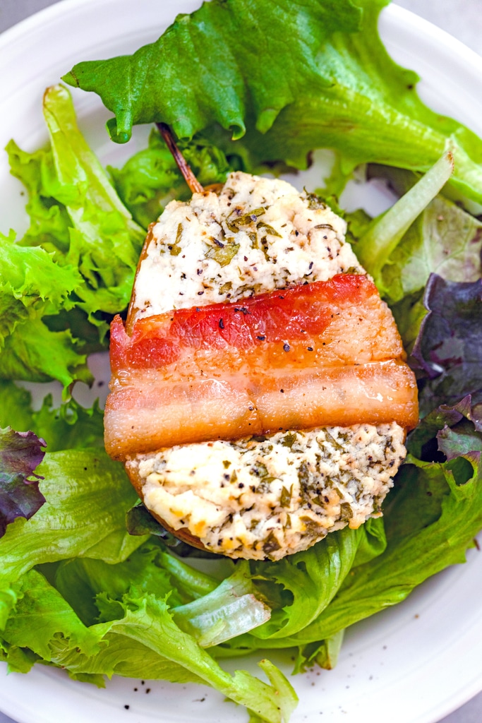 Overhead closeup view of a roasted pear with goat cheese wrapped in bacon on a bed of greens