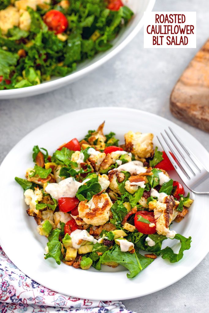 Overhead closeup view of a white bowl of roasted cauliflower BLT salad with a large bowl in the background and recipe title at top