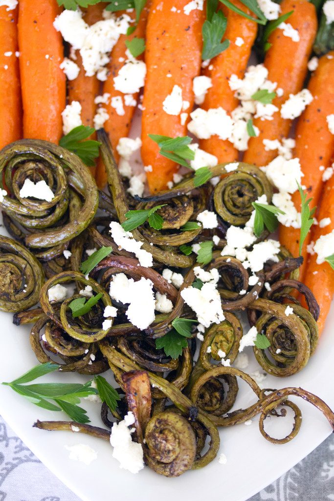 Closeup of roasted fiddleheads topped with feta cheese and parsley