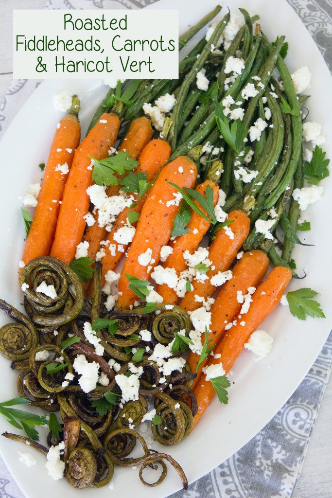 Overhead view of white platter with roasted fiddleheads, carrots, and haricot vert topped with feta cheese and parsley with recipe title at top