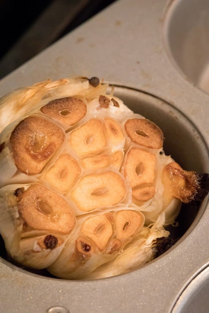 Overhead view of a head of roasted garlic in muffin tin