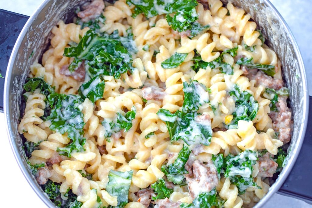 overhead view of mac and cheese with sausage and kale in saucepan