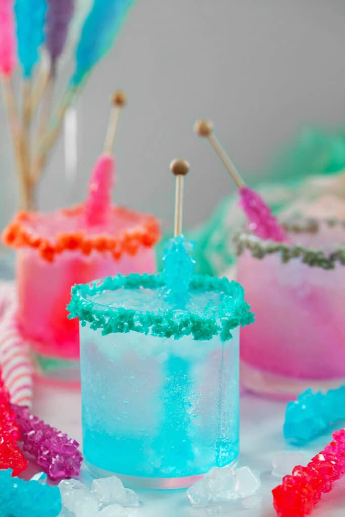 Head-on view of a blue rock candy cocktail with more cocktails and rock candy in background