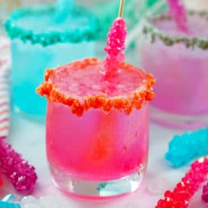 Head-on closeup view of a bright pink rock candy cocktail with blue and purple cocktails in the background