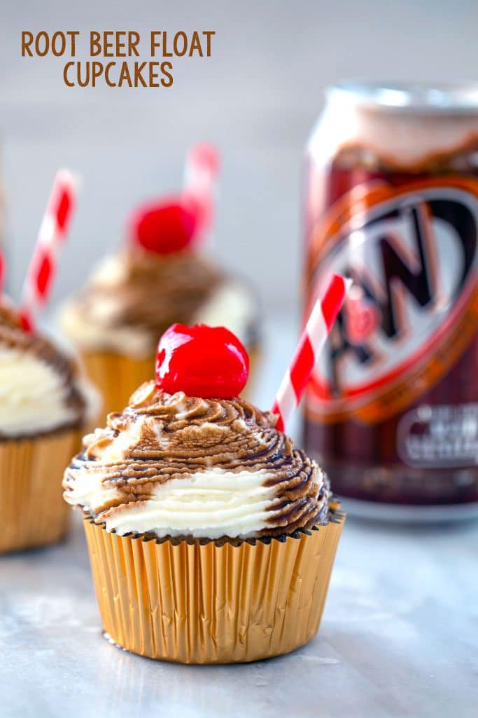 Head-on view of root beer float cupcake with red and white straw and cherry with other cupcakes and a can of root beer in the background and "Root Beer Float Cupcakes" text at top