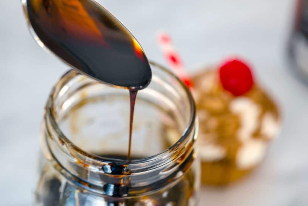 Mason jar with spoon held above it drizzling root beer syrup