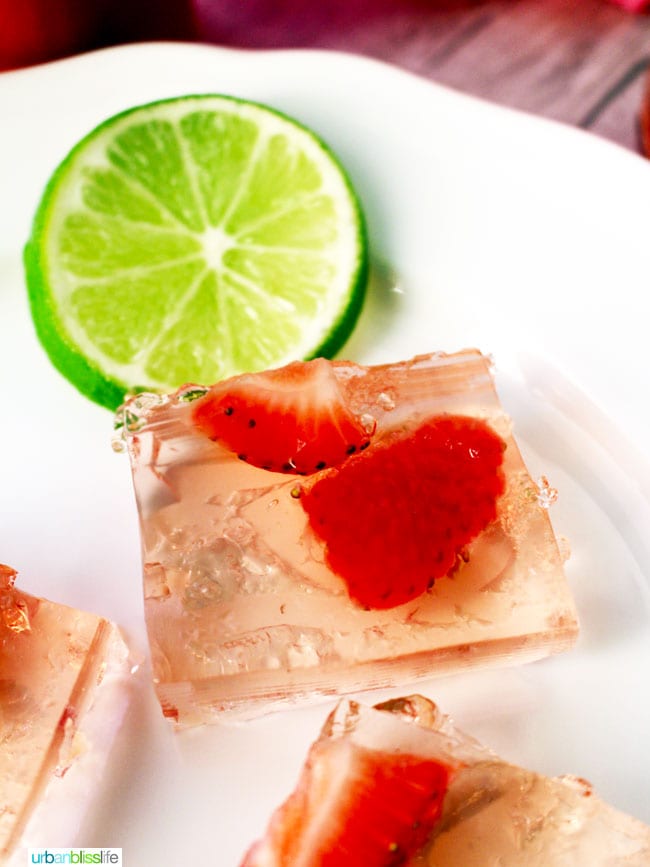 Strawberry jello shots squares on a plate with lime garnish