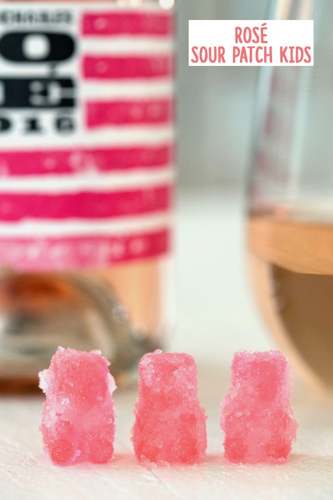 Head-on view of three rosé sour patch kids lined up with bottle and glass of rosé in the background and recipe title at top