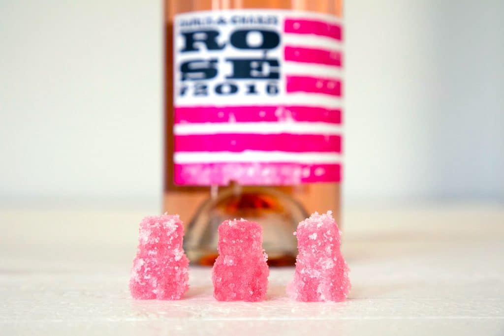 Landscape head-on view of three rosé sour patch kids with a bottle of rosé behind them