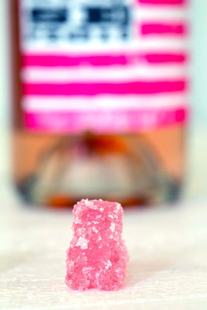 Head-on view of a single pink rosé sour patch kid with bottle of rosé behind it