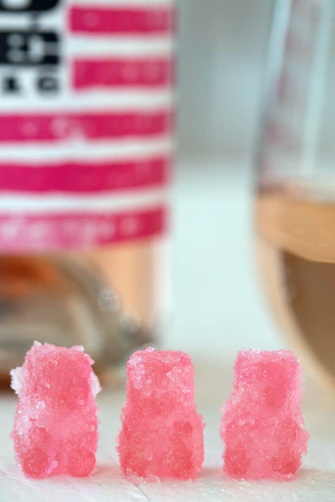 Head-on view of three rosé sour patch kids lined up with bottle and glass of rosé in the background