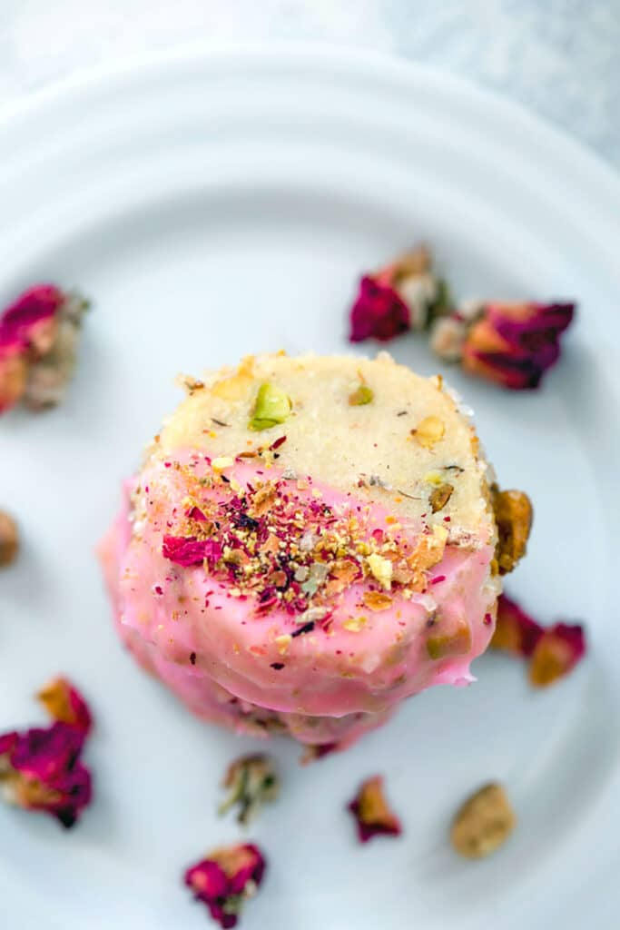 Bird's eye view close-up of a stack of rose pistachio shortbread cookies on a white plate with rose buds around