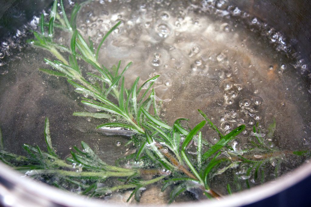 Simple syrup boiling in a saucepan with a sprig of rosemary in it