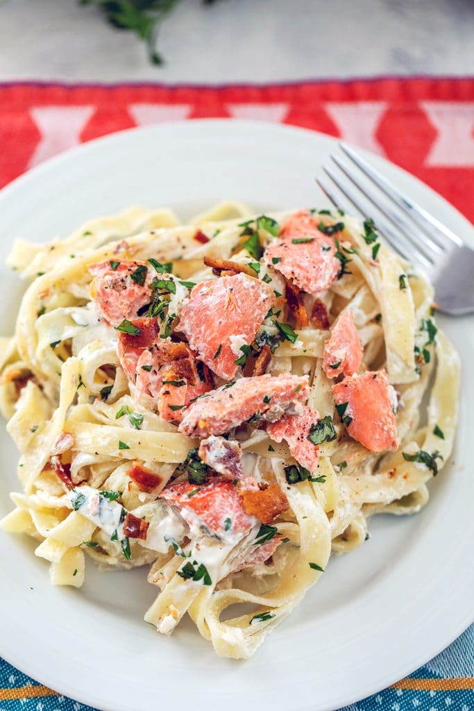 Close-up view of white plate with fettuccine, salmon, bacon, and herbs with a fork