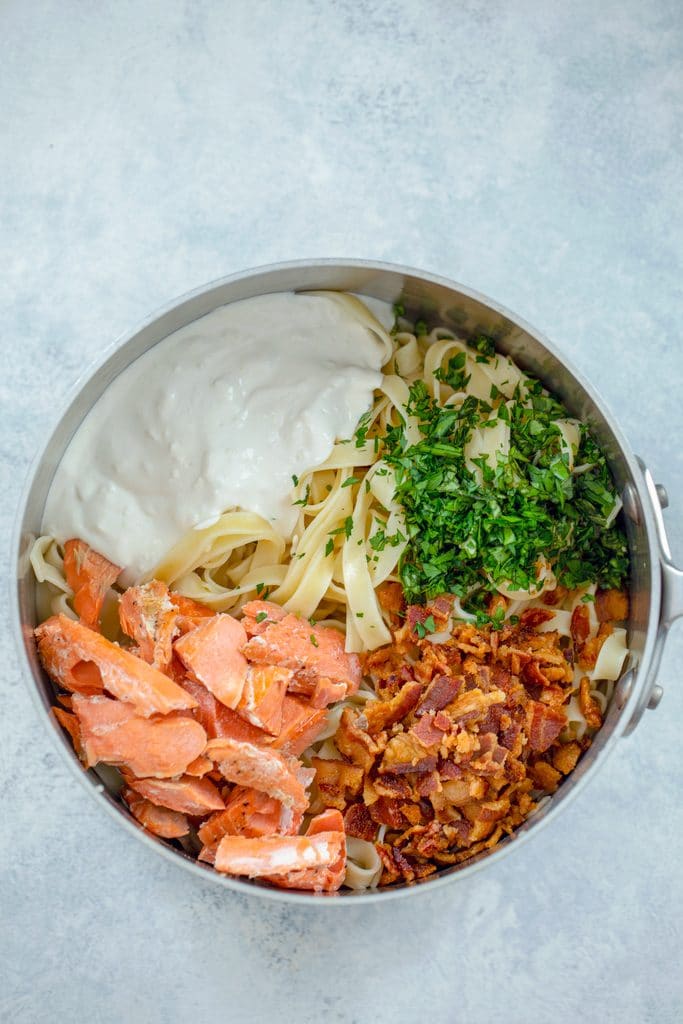 Overhead view of pot with fettuccine, salmon, sour cream caesar sauce, herbs, and bacon