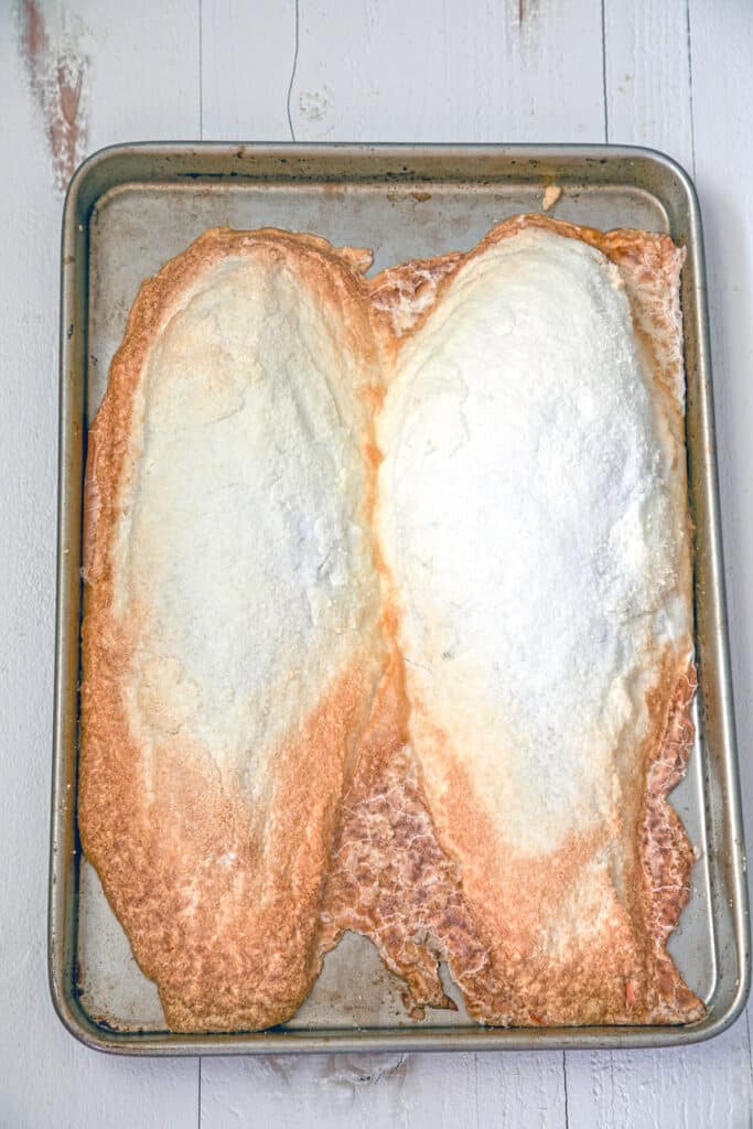 Overhead view of baking sheet with two salt-covered whole fish after baking.