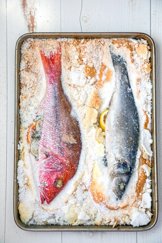 Overhead view of two fish whole on a baking pan with salt chipped away.