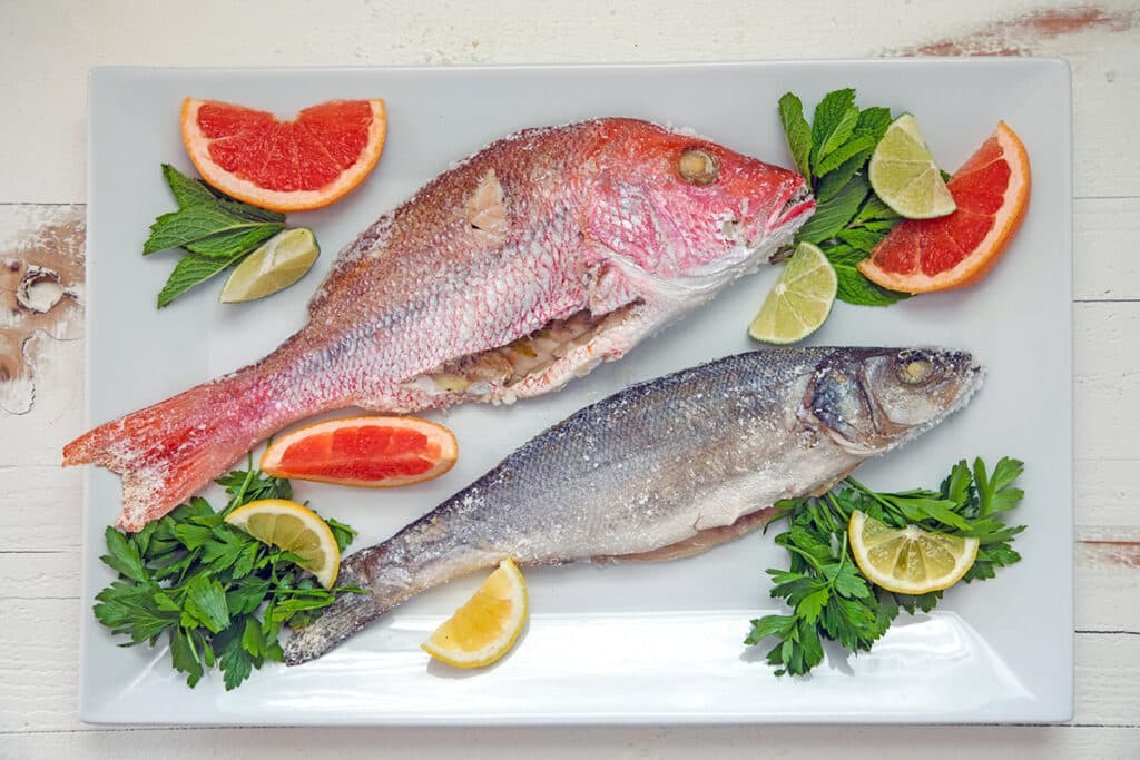 Two whole fish with salt cracked off on a serving platter.