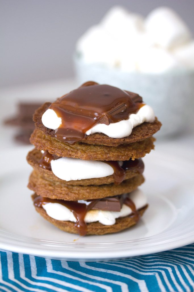 Head-on view of salted caramel cookie s'mores stacked on top of each other with bowl of marshmallows in background