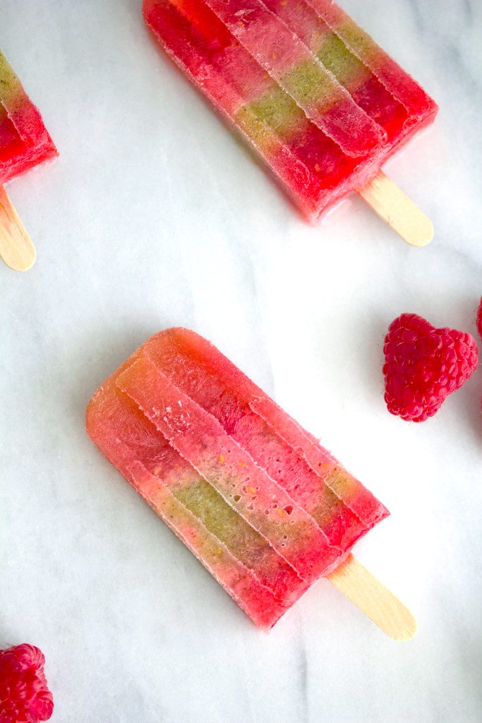 Overhead view of multiple raspberry kiwi sangria popsicles on a marble surface with raspberries