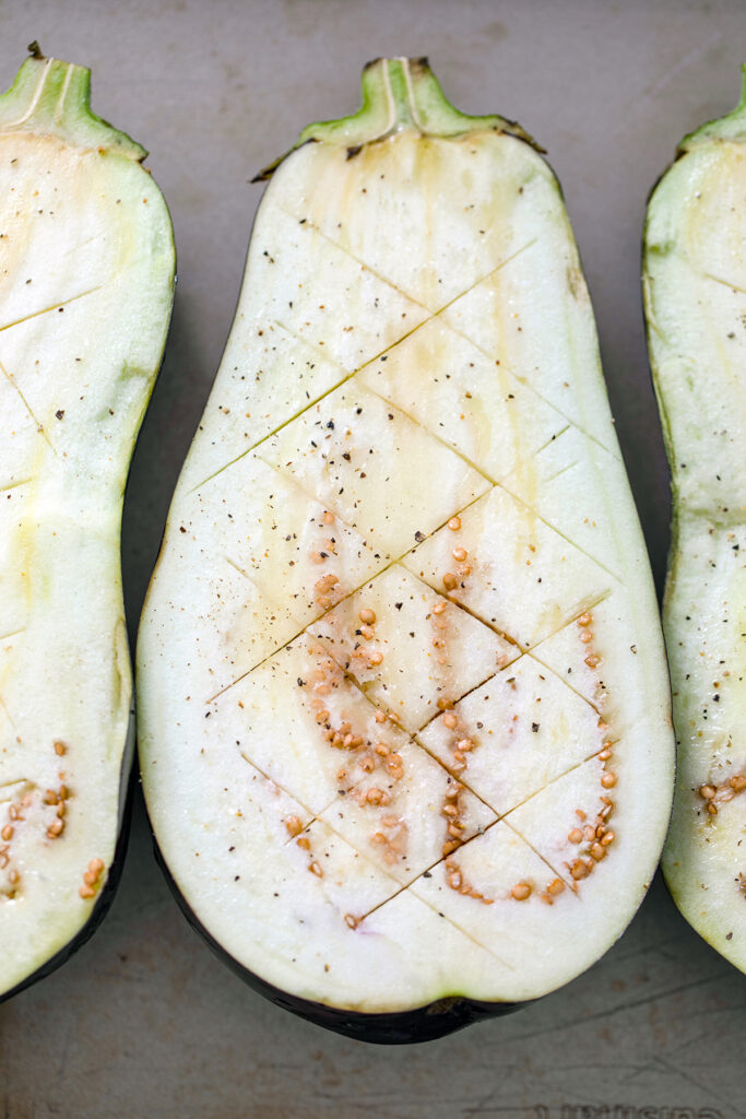 Overhead view of scored eggplant halves with zigzag cuts in them and salt and pepper.