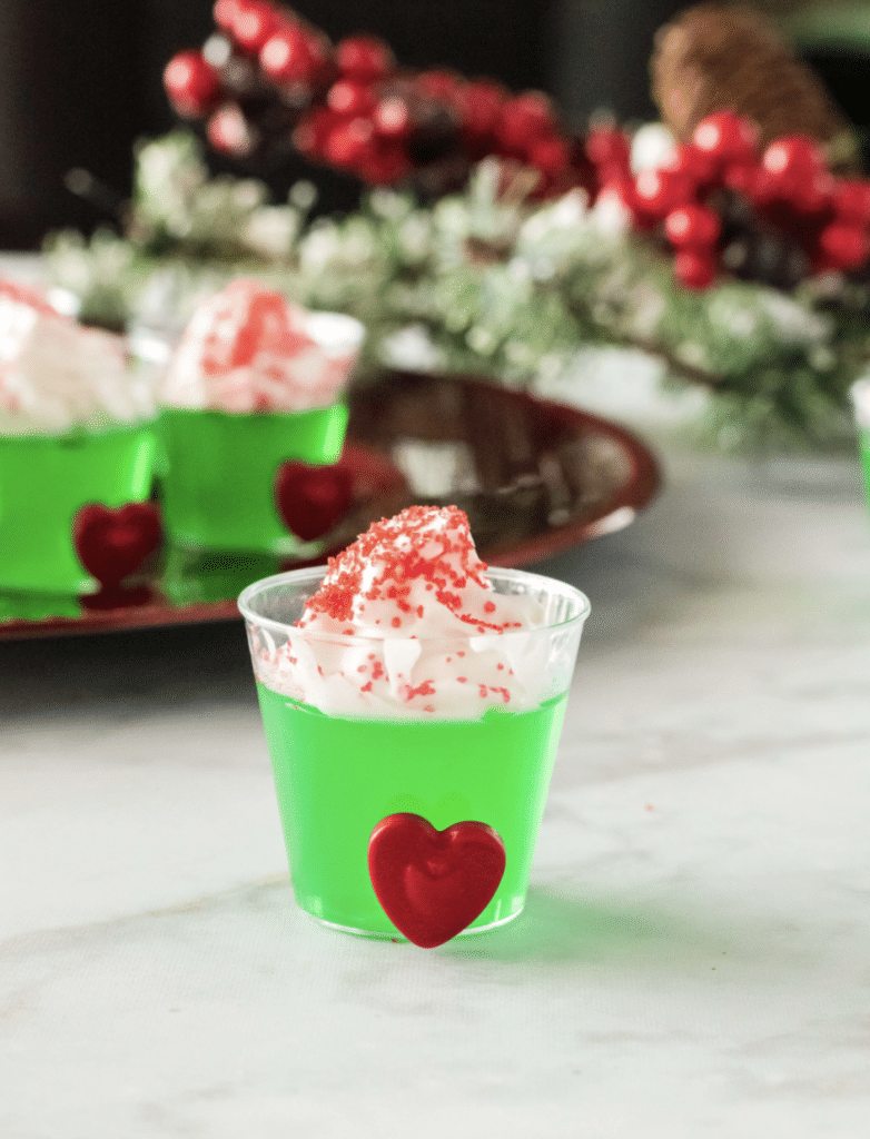 Green Grinch jello shots in little cups with whipped cream and red hearts