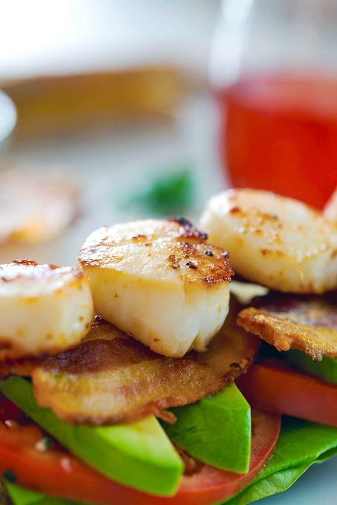 Close-up of seared scallops sitting on top of bacon, avocado, tomato, and lettuce