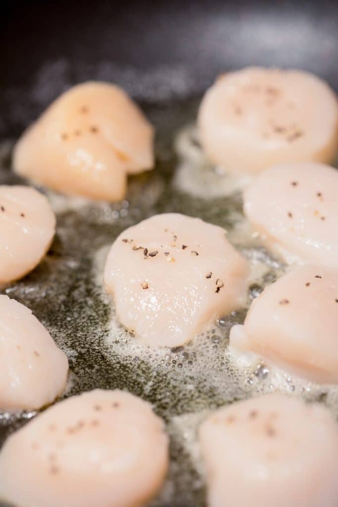 Scallops in a pan being seared in butter and olive oil mixture
