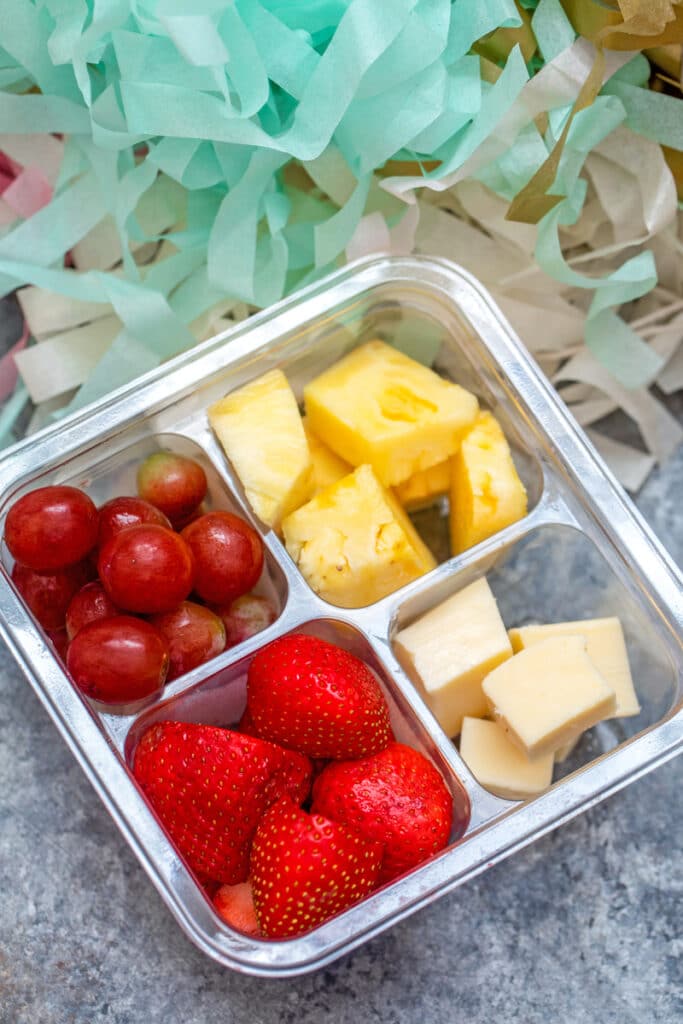 Overhead view of a snack pack featuring strawberries, grapes, pineapple, and cheese