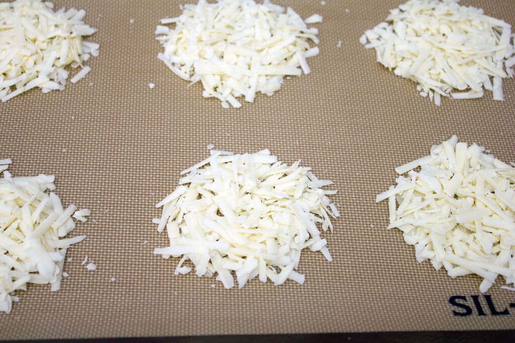 Overhead view of multiple piles of shredded cheddar cheese on a Silpat