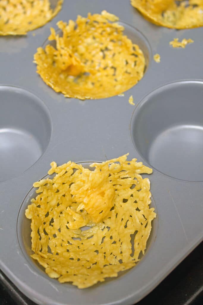 Overhead view of cheese discs being shaped in muffin tin