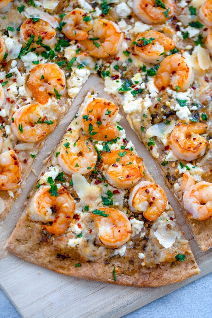 Overhead view of shrimp scampi pizza on wooden board with a slice pulled out.