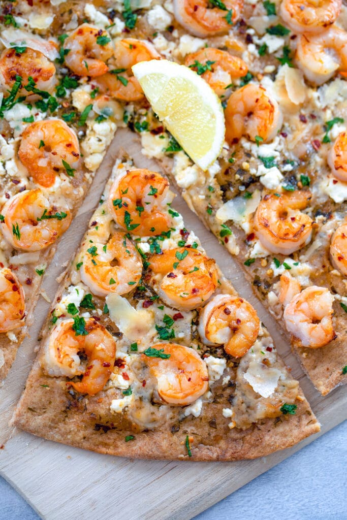 Overhead view of shrimp scampi pizza with a lemon in the center and a sliced pulled out on top of a wooden board