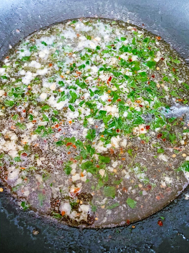 Overhead view of parsley, wine, and lemon juice added to skillet with garlic