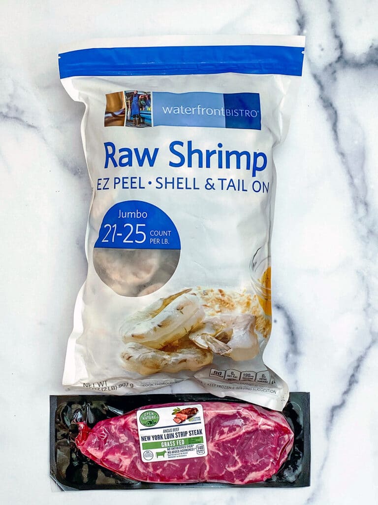 View of frozen jumbo shrimp in a bag and NY strip steak.