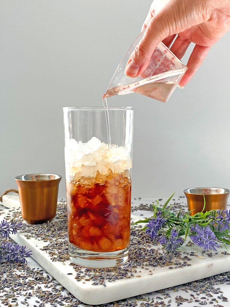 Lavender simple syrup being poured into coffee in ice-filled glass