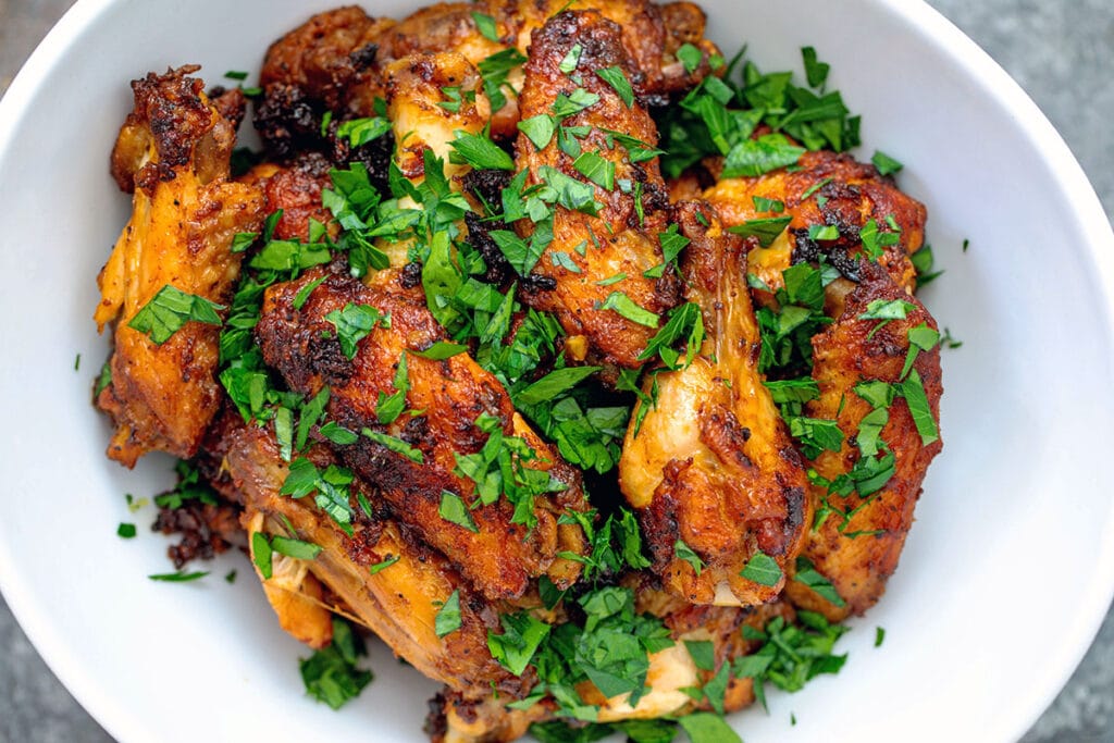 Landscape overhead view of garlic chicken wings in a white bowl topped with chopped parsley