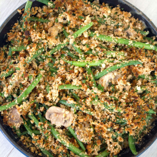 Overhead closeup view of healthy skillet green bean casserole with mushrooms and breadcrumb topping in a blue skillet on white surface