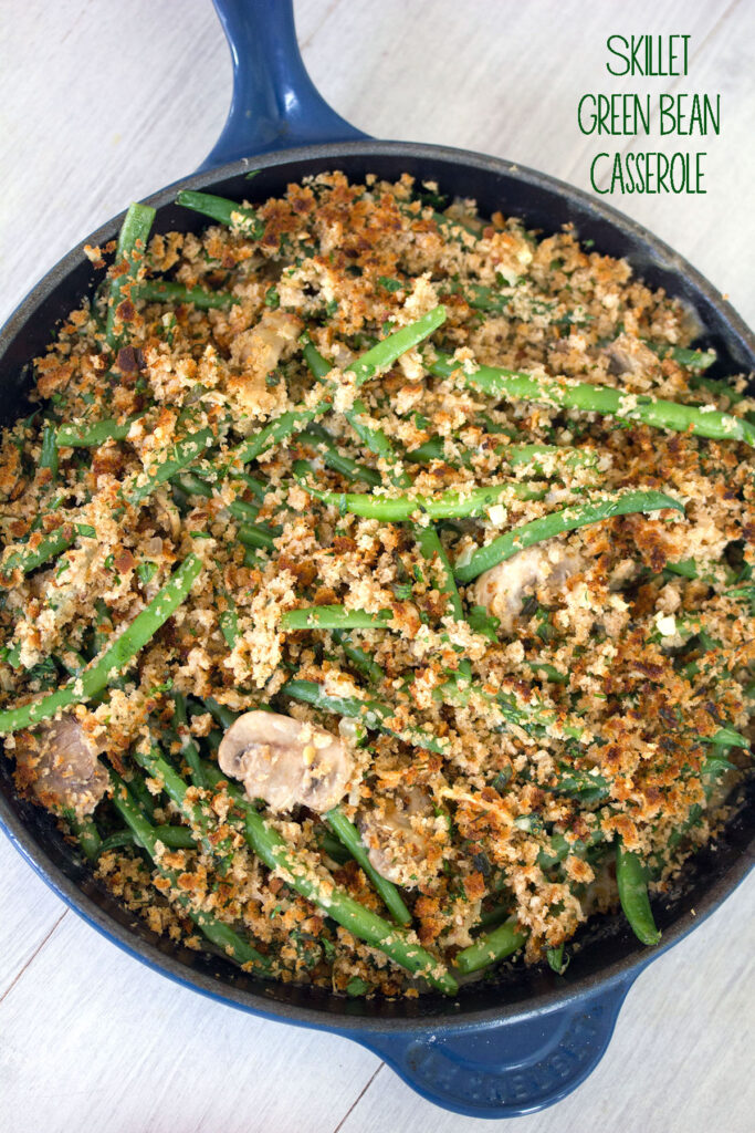 Overhead view of healthy skillet green bean casserole with mushrooms and breadcrumb topping in a blue skillet on white surface with recipe title at top of image