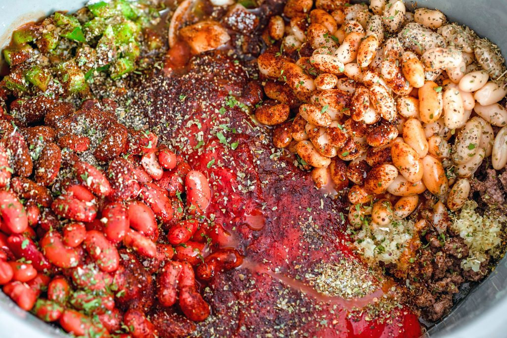 Overhead view of chili ingredients, including beans, tomatoes, beef, garlic, and peppers all in slow cooker